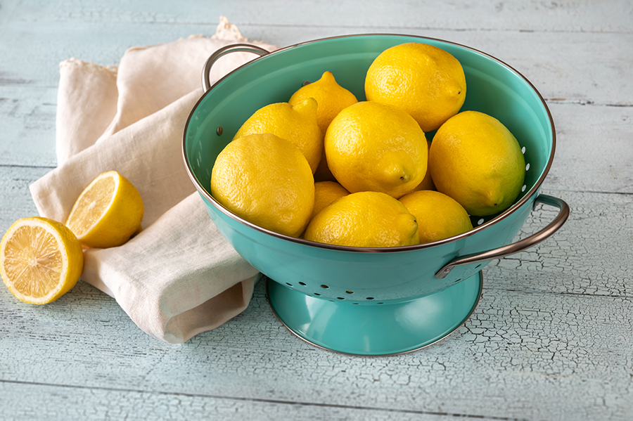 Fresh lemons in blue colander. Wooden background